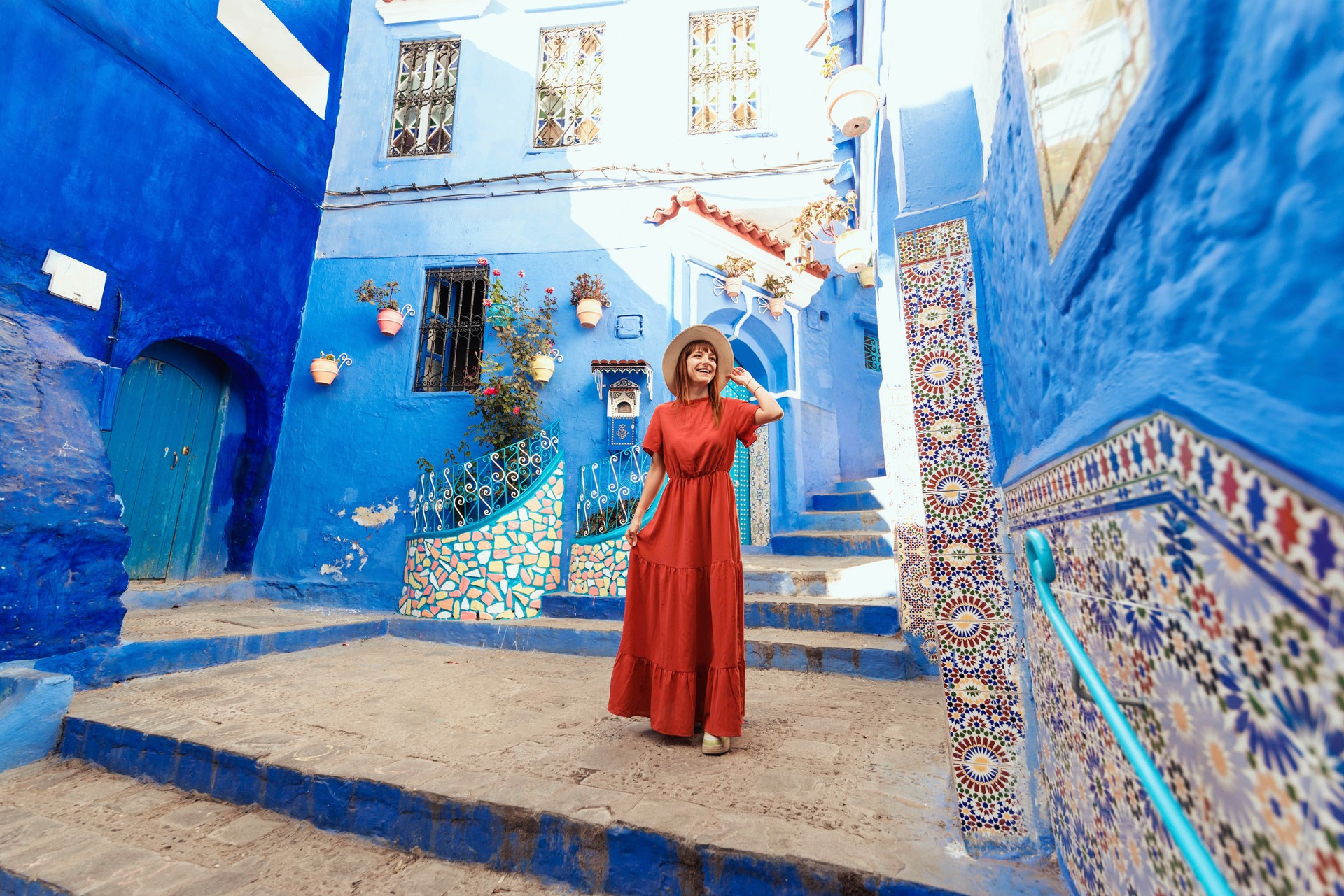 Young woman with red dress visiting the blue city Chefchaouen, Marocco - Happy tourist walking in Moroccan city street - Travel and vacation lifestyle concept